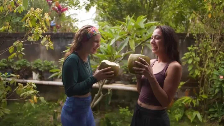 Two team members laughing together with fresh coconuts in a garden — connection in person