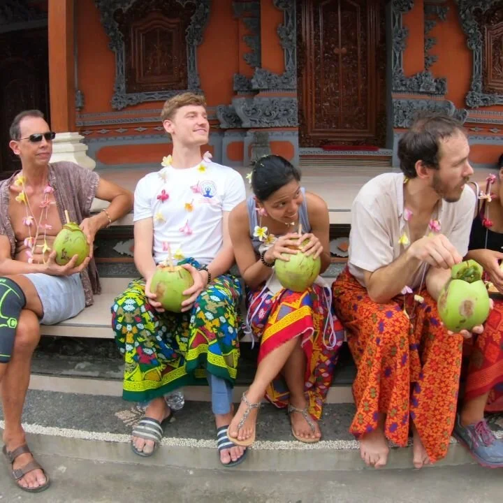 A team sharing fresh coconuts on temple steps in beautiful traditional clothes